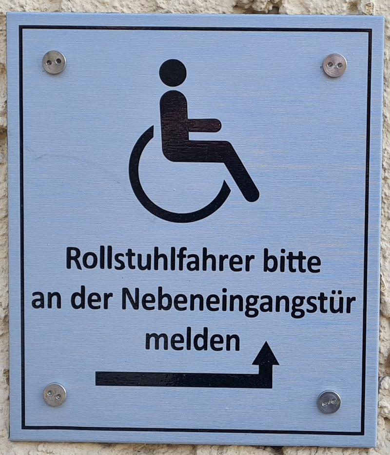 Hinweisschild am Haupteingang das auf den Rollstuhlgerechten Eingang an der Seite des Amtsgerichts verweist